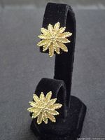 Front view of both gold tone starburst earrings on stand