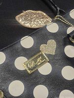Close-up of gold-tone Betsey Johnson plaque, glitter lips charm, polka dot and heart pattern