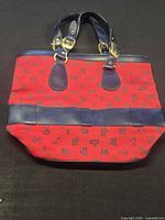 Full view of red zodiac print handbag with dark leather trim and handles
