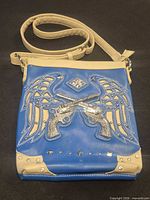 Front of blue faux leather purse with beige trim and rhinestone, wing and revolver design