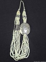 Full view of multi-strand cream seed bead necklace with hammered oval pendant