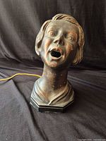 Front view of metal bust lamp showing facial features and cord
