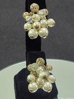 Front view of both clip-on earrings displaying clustered faux pearls and filigree elements