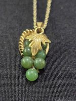 Close-up of pendant showing gold-tone leaf, vine detail and six green beads