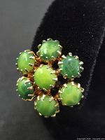 close-up of one earring showing green cabochons and prong settings