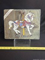 Front view of full slate plaque with painted carousel horse, New Orleans text, leather strap and ruler for scale