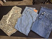 Three pairs of pants displayed flat: leopard print, blue denim pair with Levi’s patch, blue distressed denim pair