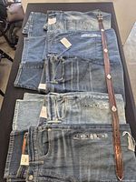 Five pairs of blue jeans stacked with brown belt alongside