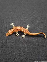 Full view of orange and gold-tone lizard brooch on dark fabric background