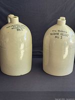 Two cream stoneware jugs side by side showing overall appearance and stencilled lettering