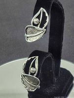 Front view of both silver leaf motif earrings on stand