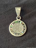 Front view of pendant showing Aztec calendar design and abalone inlay