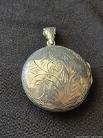 Front view of round sterling silver floral-engraved locket with bail