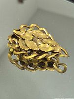 front view of gold-tone leaf brooch on reflective surface
