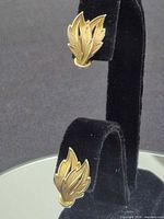 Front view showing both gold-tone leaf earrings on display stand