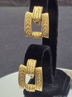 Full view of both gold-tone hinged clasp earrings on stand
