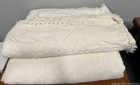 Two stacked cream woven bedspreads showing pattern and fringe