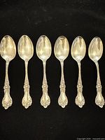 Full view of six matching ornate sterling silver spoons aligned on dark background