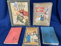 Group shot of all five antique children’s books laid out on blue background