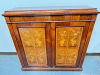 Front view of two-door wood cabinet showing floral marquetry panels and geometric inlay