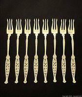 Eight identical sterling silver cocktail forks laid out tines up, showing ornate filigree handles.