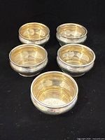 Five sterling silver open salt cellars with gilt interiors arranged on black background.