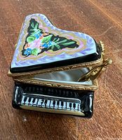 Open porcelain piano trinket box showing floral-painted lid, keyboard front and white interior with gold hinge