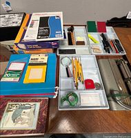 Overall view of lot showing hole punch, organizer trays with contents, drafting compasses, Avery labels, file folders, paper pad