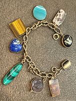 Overall view of gold link bracelet with nine assorted gemstone charms displayed flat