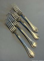 Four Birks sterling silver dinner forks laid out, showing pattern and monograms