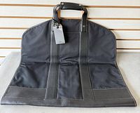 Full view of folded black leather garment bag with handles and tag