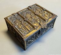Closed brass casket showing Gothic relief panels