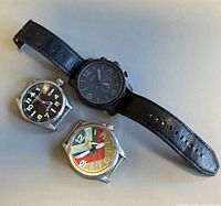 Three watches laid out: Stührling head, Fossil Nate chronograph with strap, Fossil multicolour dial head