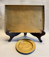 Rectangular brass tray upright on stand with round brass plate in front