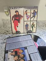 Front album cover on stand, inner sleeve displayed, vinyl record partially visible