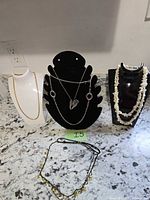 Three necklace busts showing gold-tone chain, silver-tone heart pendant necklace, and shell chip strand, plus two necklaces on counter
