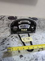 Packaged novelty sign with tape measure showing width about 5.5 inches