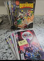 Front view of two stacks of 15 comic books; The Outsiders and Bloodline: Daughter of Blade covers visible