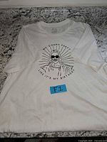 Full view of folded white graphic T-shirt with blue lot sticker