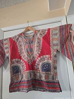 Front view of red patterned V-neck shirt on hanger