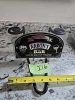 Front view of metal sign showing graphics and integrated hook with measuring tape for scale