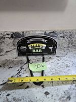 Front view of packaged Alan's Bar sign beside measuring tape