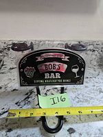 Front of black metal Bob's Bar sign showing graphics, suction cups and hook with tape for scale