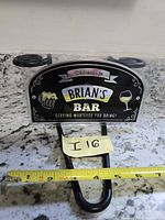 Front view of packaged Brian's Bar metal sign showing graphics and hook