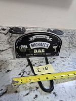 Front view of packaged Michael's Bar sign with measuring tape showing width