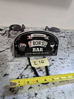Front view of "Ron's Bar" sign with tape measure showing width