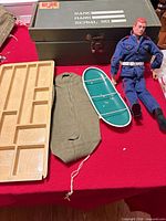 Lot overview: action figure, surfboard accessory, storage trunk, wooden tray on red surface