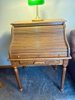 Front view of closed roll-top desk showing tambour, keyhole, drawer, and turned legs
