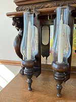 Front view of both matching dark stained wood wall sconces with glass chimneys and candle sockets