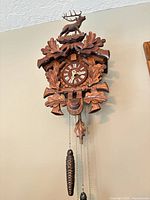 Front view of carved cuckoo clock showing stag crest, oak leaves, dial, weights and pendulum